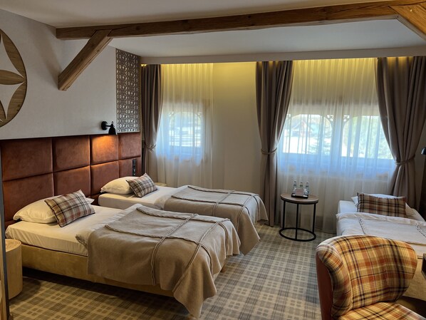 Habitación de hotel con dos camas, una mesita redonda con botellas, un sillón de estampado escocés y un adorno en la pared.