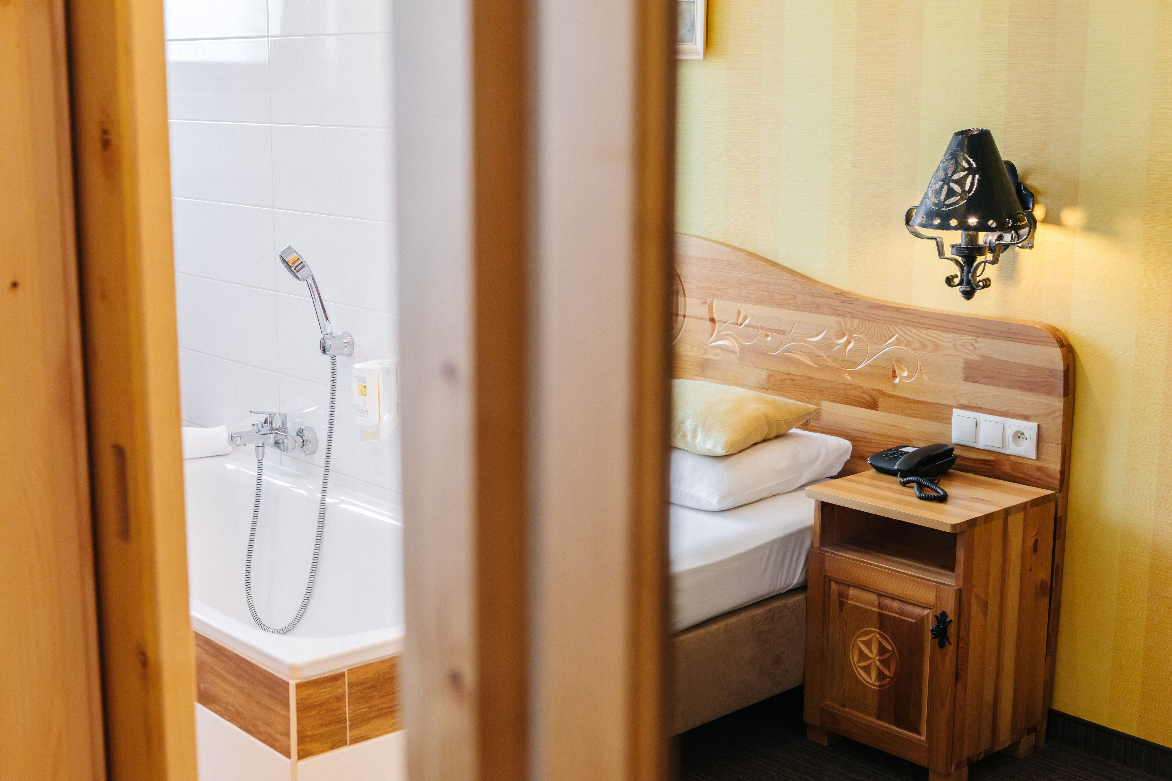 A hotel room with a wooden headboard, a bedside table with a lamp, a bed with white bedding, and a wooden nightstand.