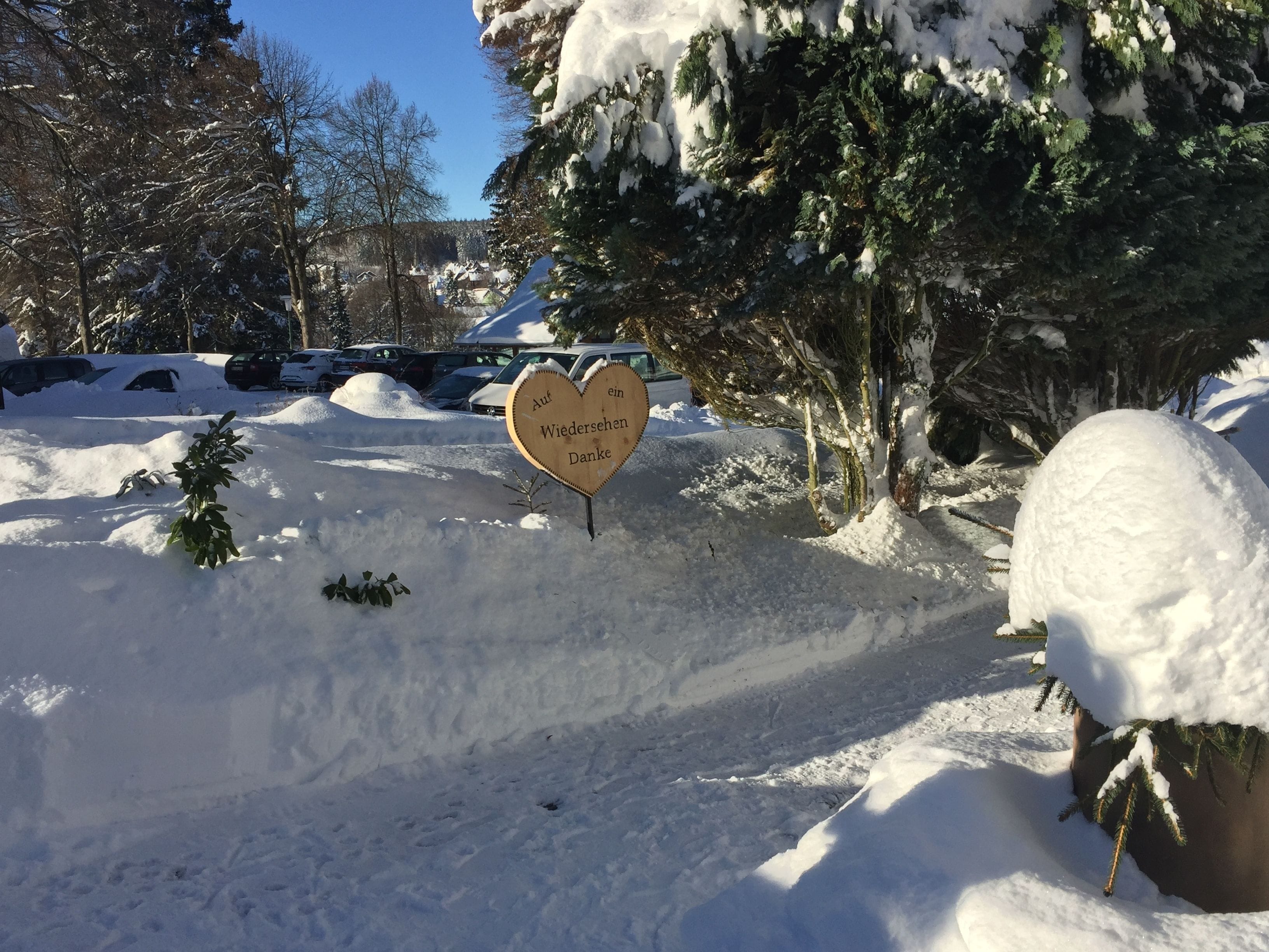 A snow-covered landscape with a heart-shaped sign reading "Auf Wiedersehen Danke" in a parking lot.