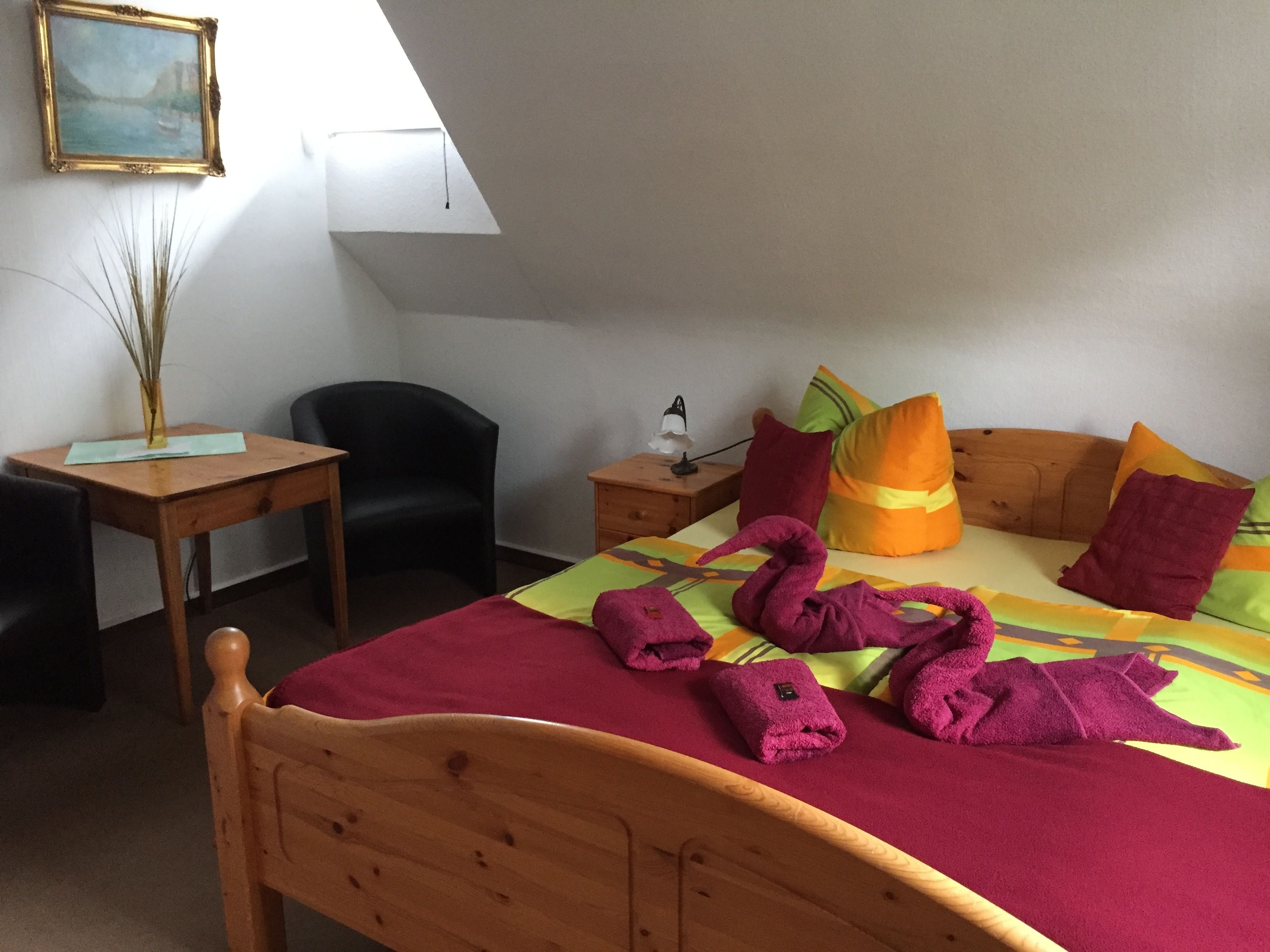 Ein Schlafzimmer mit einem hölzernen Bett, einem Schreibtisch, einem Stuhl, einem Nachttisch mit Lampe und einem Gemälde an der Wand.