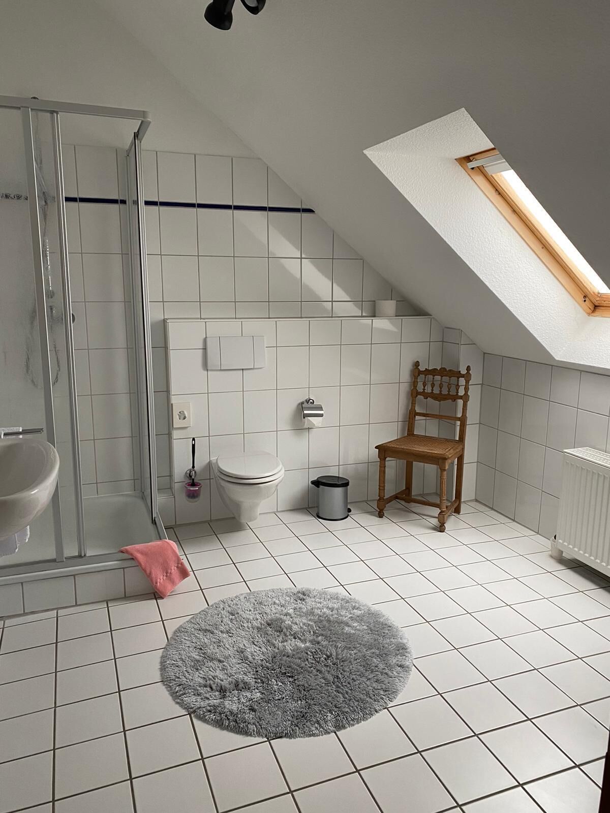 Un bagno moderno con doccia, wc e una sedia in legno.