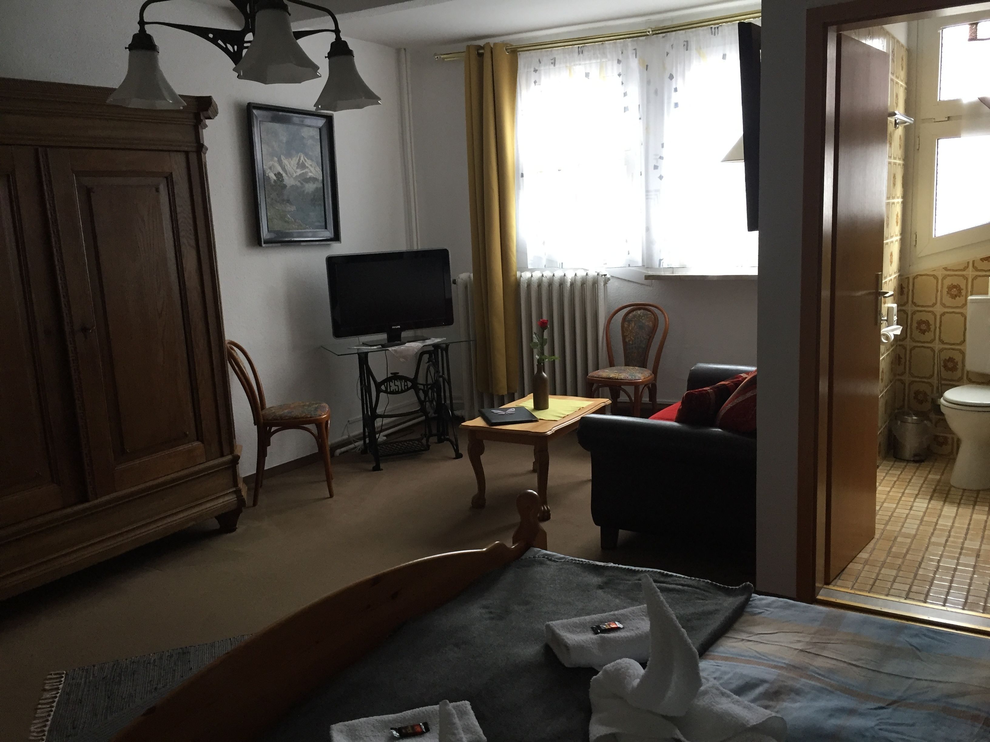 A hotel room with a bed, a TV on a stand, a chair, a sofa, a cabinet, and a window with curtains.