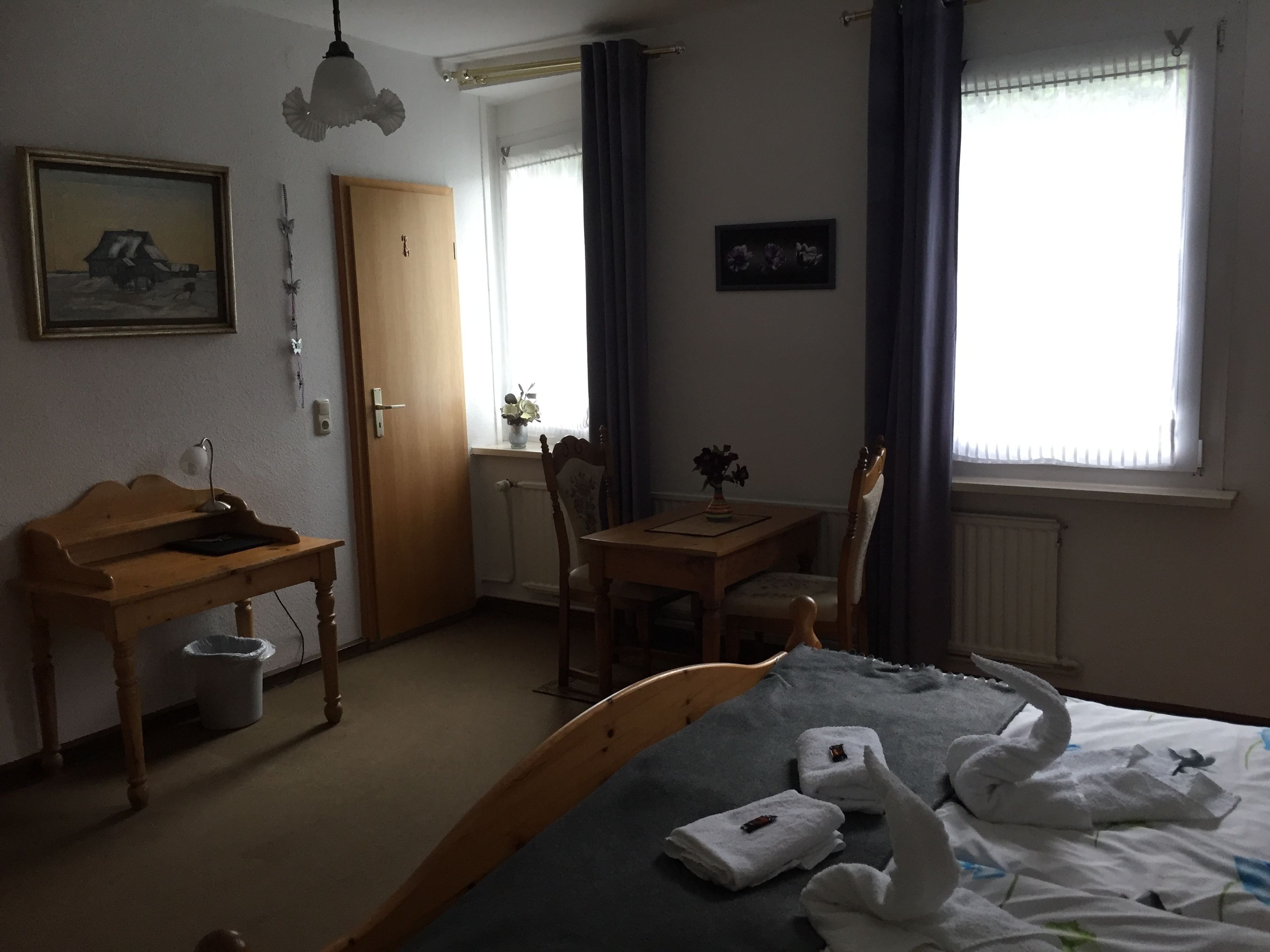 A hotel room with a bed, a wooden desk, a chair, a table, and a radiator.