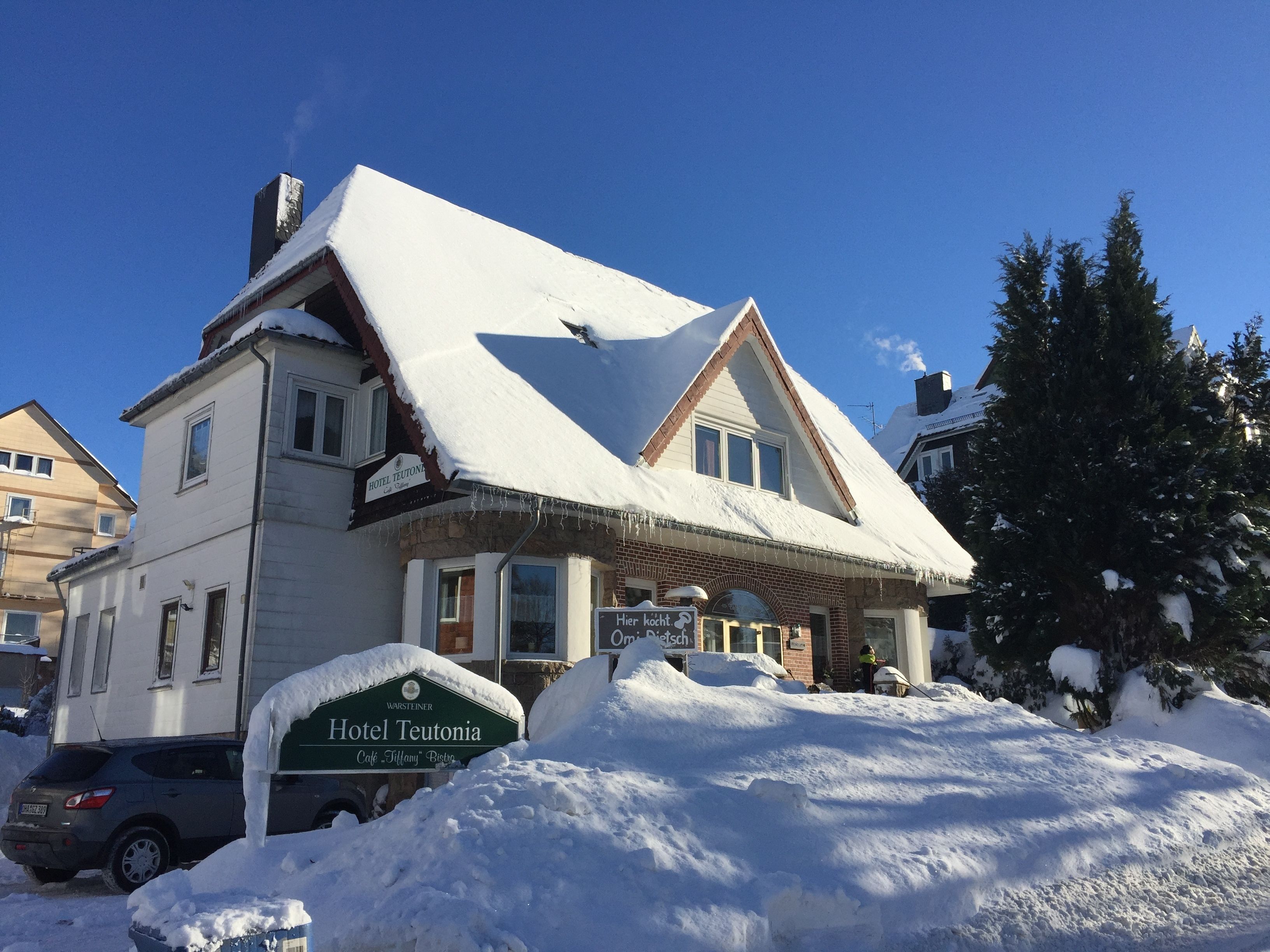 Ένα διώροφο κτίριο με χιονισμένη στέγη και μια πινακίδα που αναγράφει «Ξενοδοχείο Τευτόνια».