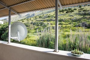 A balcony with a satellite dish, a potted plant, and a view of a grassy hillside with rocks. - Sv. Jelena apartments (Pag)
