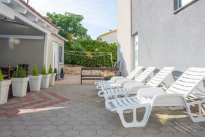 A patio with white lounge chairs, potted plants, and a stone wall. - Sv. Jelena apartments (Pag)