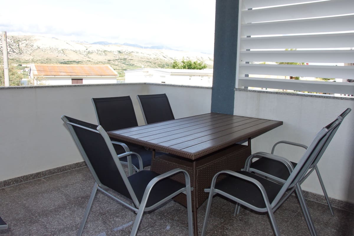 A balcony with a table and chairs, offering a view of a mountainous landscape.