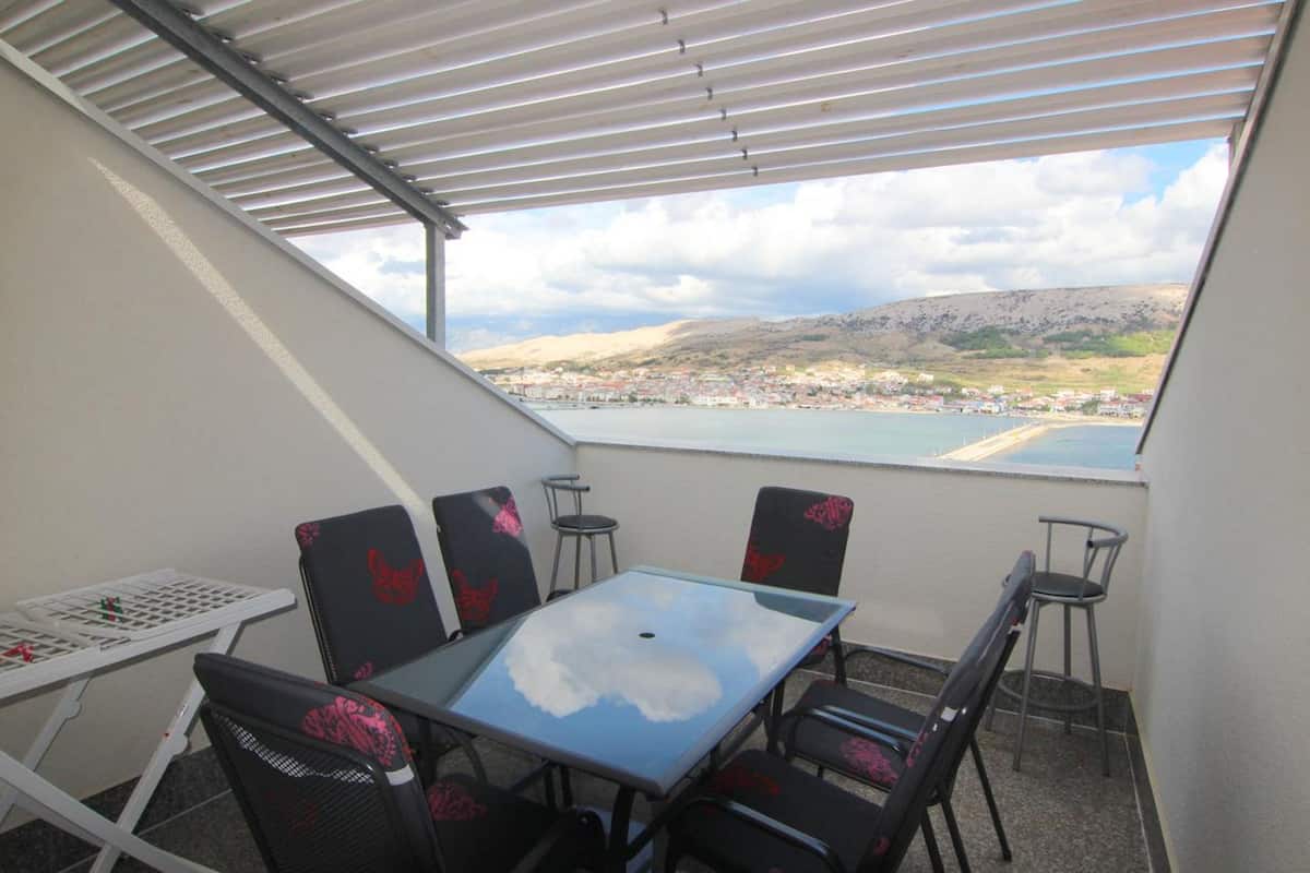 A balcony with a table and chairs, overlooking a body of water and a town.