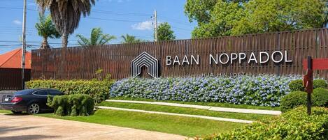 A residential area with a wooden fence, a car, and a sign that reads 'BAAN NOPPADOL.'