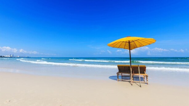 A beach with a wooden bench and a yellow umbrella. - Baan Noppadol Hua Hin Loft Hotel (Hua Hin)