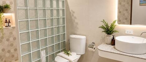 A modern bathroom with a glass shower enclosure, a toilet, a sink with a marble countertop, and a mirror above the sink.