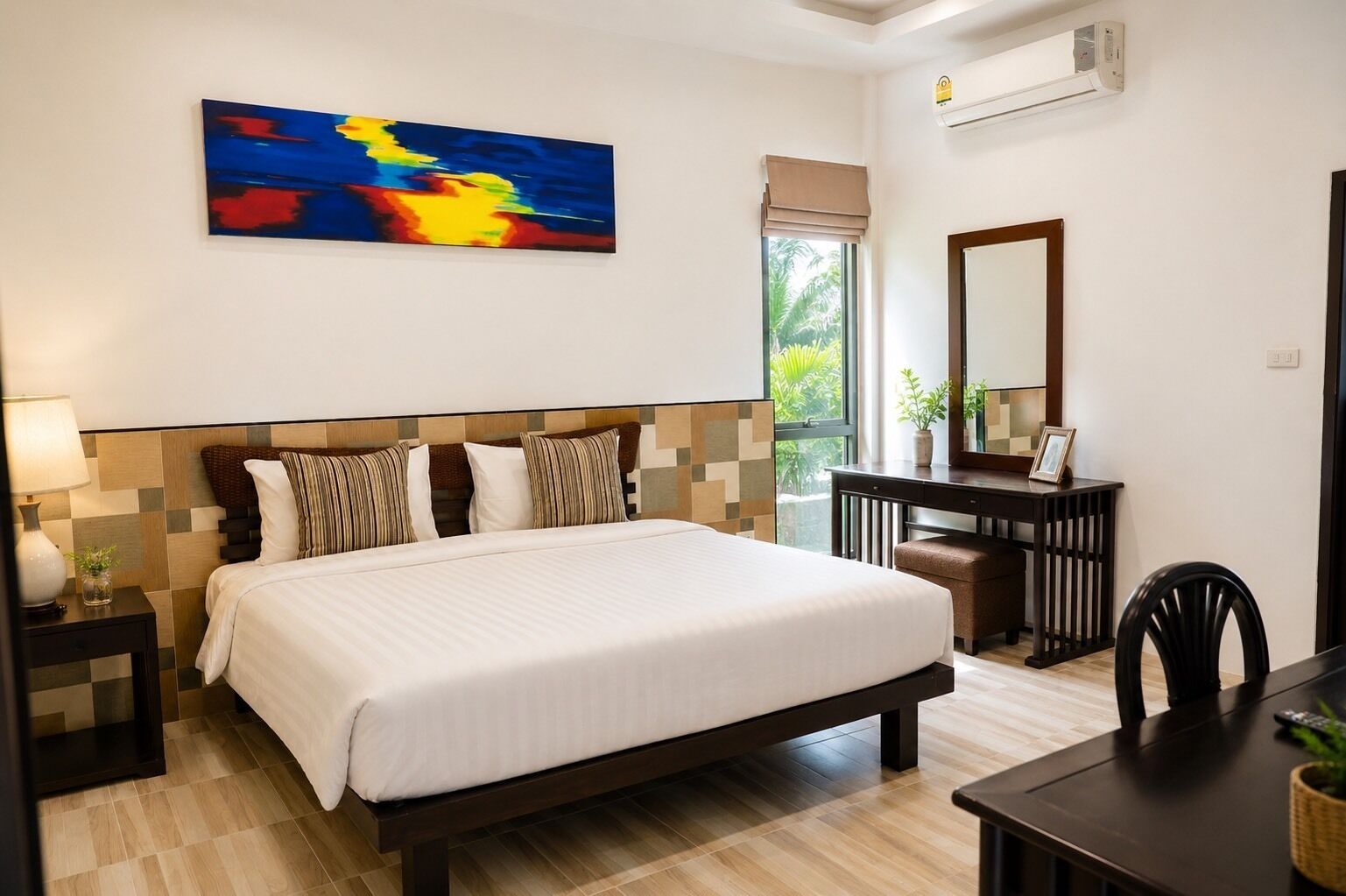 Habitación de hotel con cama, mesita de noche, lámpara, escritorio, silla y un ventanal grande.