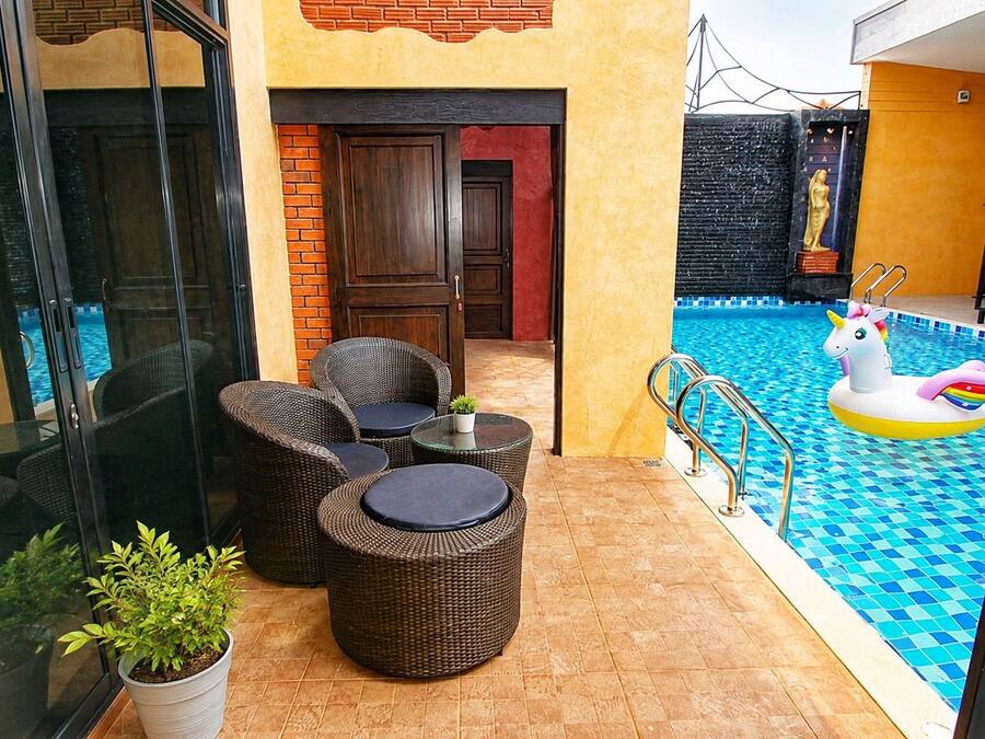 A poolside area with wicker furniture, a glass table, and a pool with a unicorn float.
