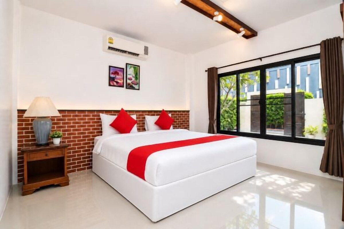 A hotel room with a large bed, a nightstand, a lamp, and a window with curtains.