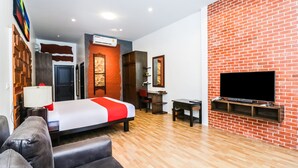A modern hotel room with a brick accent wall, a flat-screen TV mounted on the wall, a bed with a red and white bedspread, a wooden floor, and a seating area with a sofa and armchairs. - Baan Noppadol Hua Hin Loft Hotel (Hua Hin)