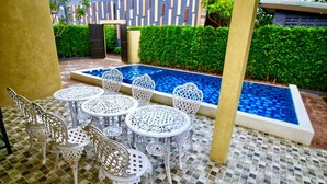 A pool area with white metal chairs and tables, surrounded by a tiled floor and a low hedge. - Baan Noppadol Hua Hin Loft Hotel (Hua Hin)