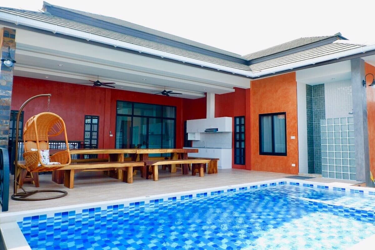 Ett modernt hus med en swimmingpool, trämöbler och en röd fasad.