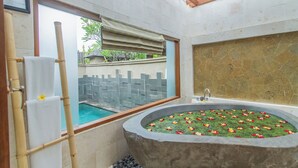 Een badkamer met een stenen badkuip, een raam met uitzicht op een zwembad en een bamboe handdoekhouder.