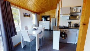 Une cuisine compacte équipée d’un lave-linge, un coin repas avec une table et des chaises, et une grande fenêtre avec des rideaux.