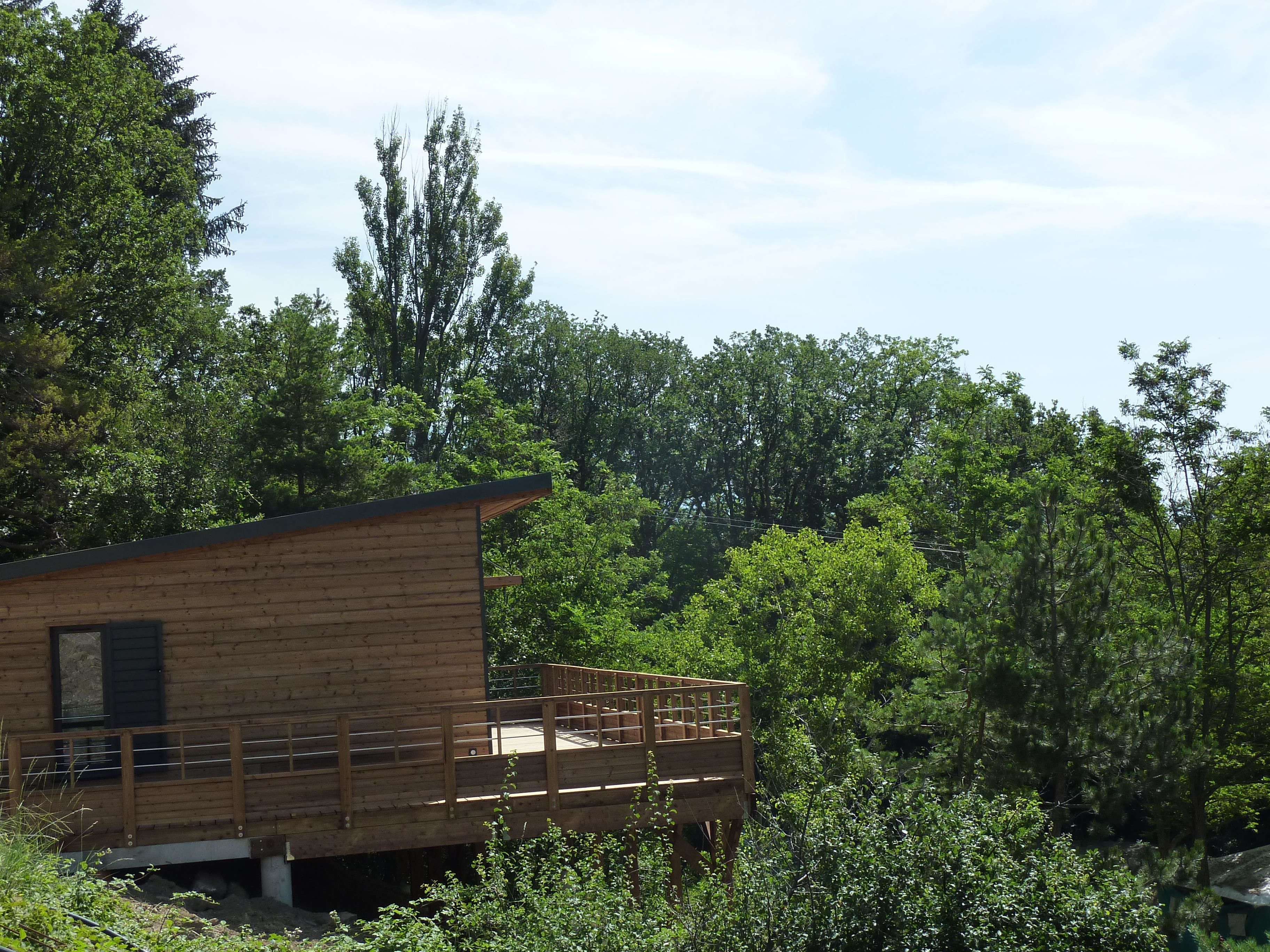 A wooden cabin with a balcony, surrounded by dense forest.