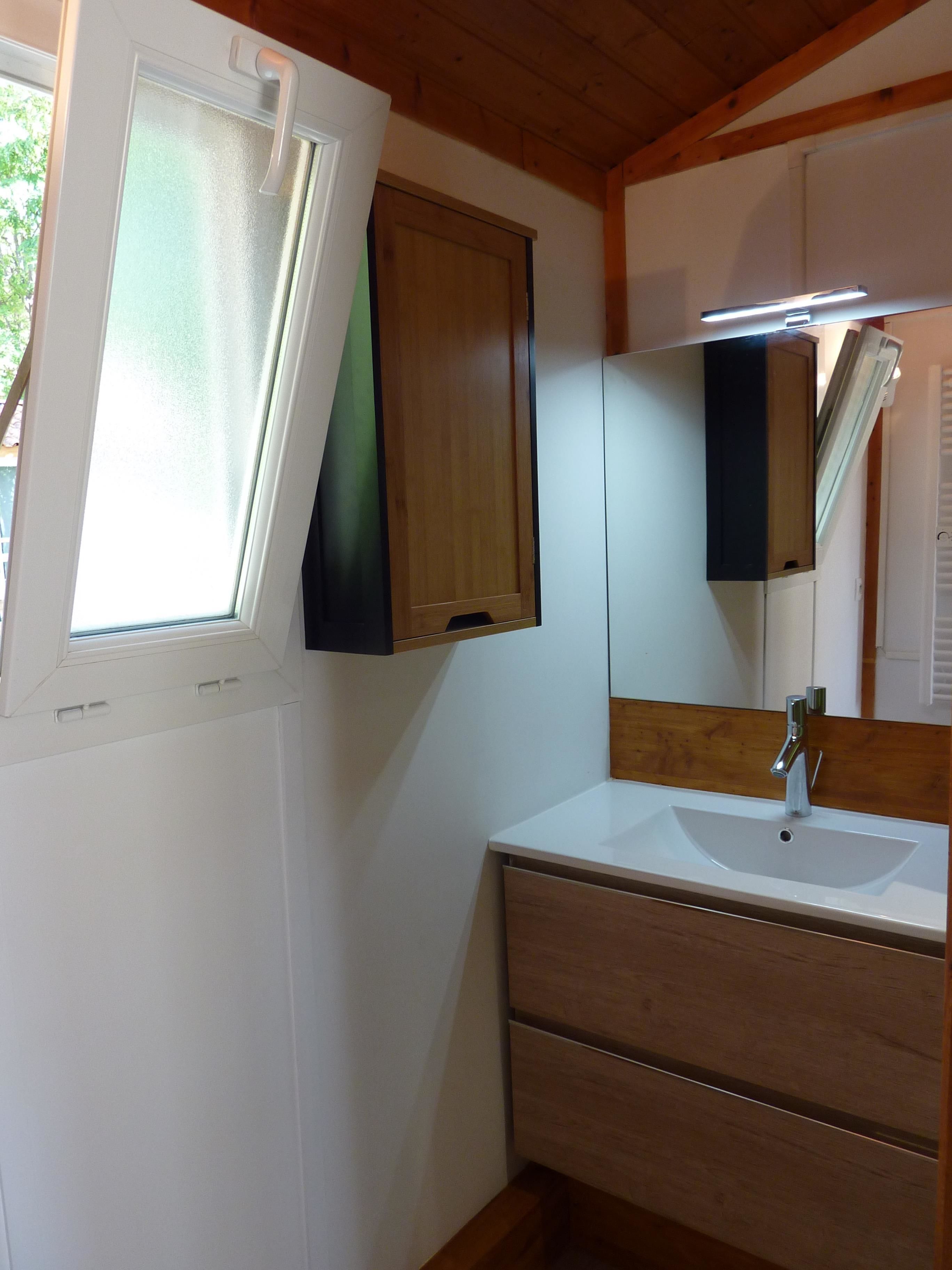 A bathroom with a white sink, wooden vanity, a mirror, and a window with frosted glass.