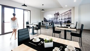 Un comedor moderno con mesas y sillas, un ventanal grande y un mural de un edificio en la pared.
