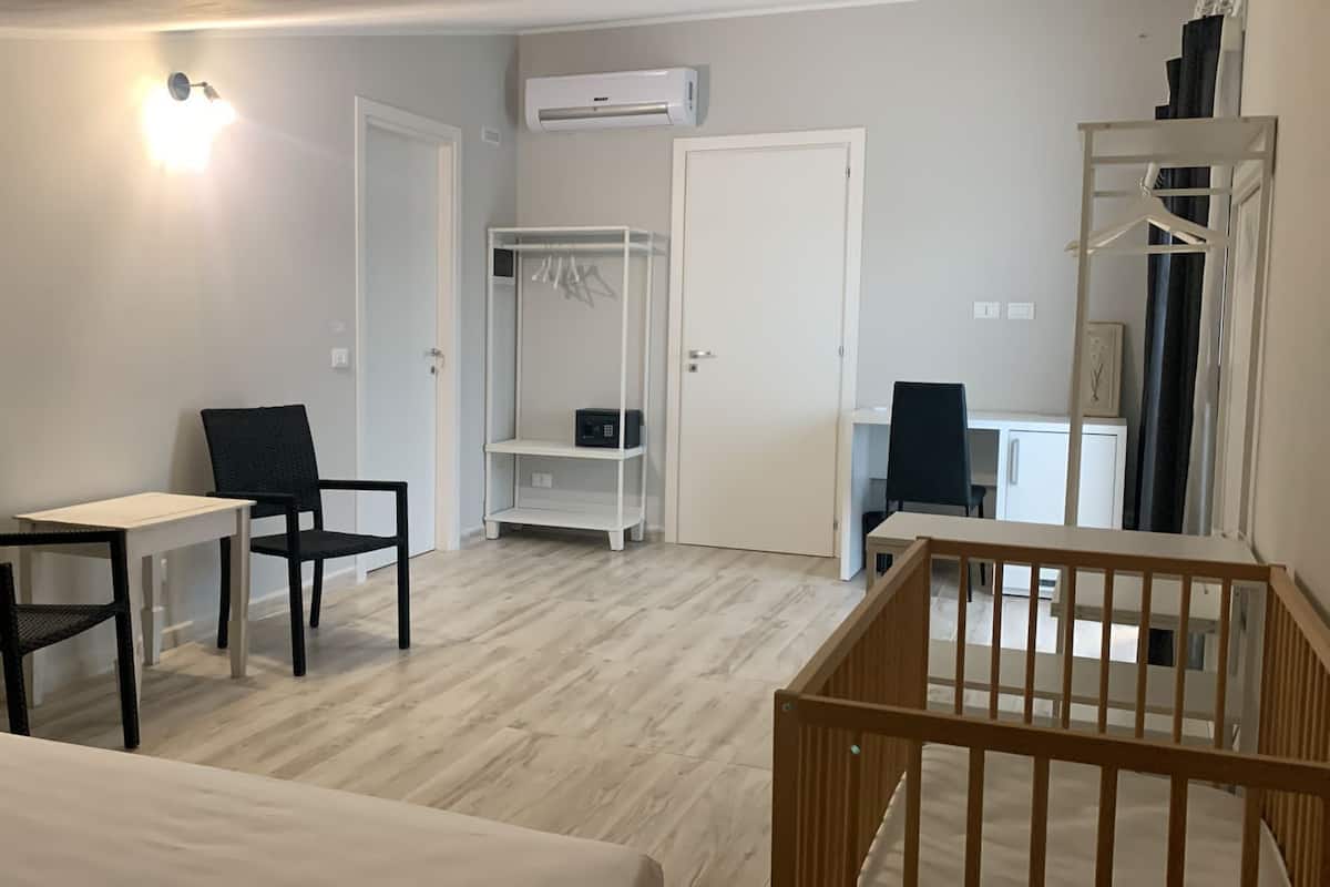 A room with a bed, two chairs, a small table, a wardrobe, and a crib.