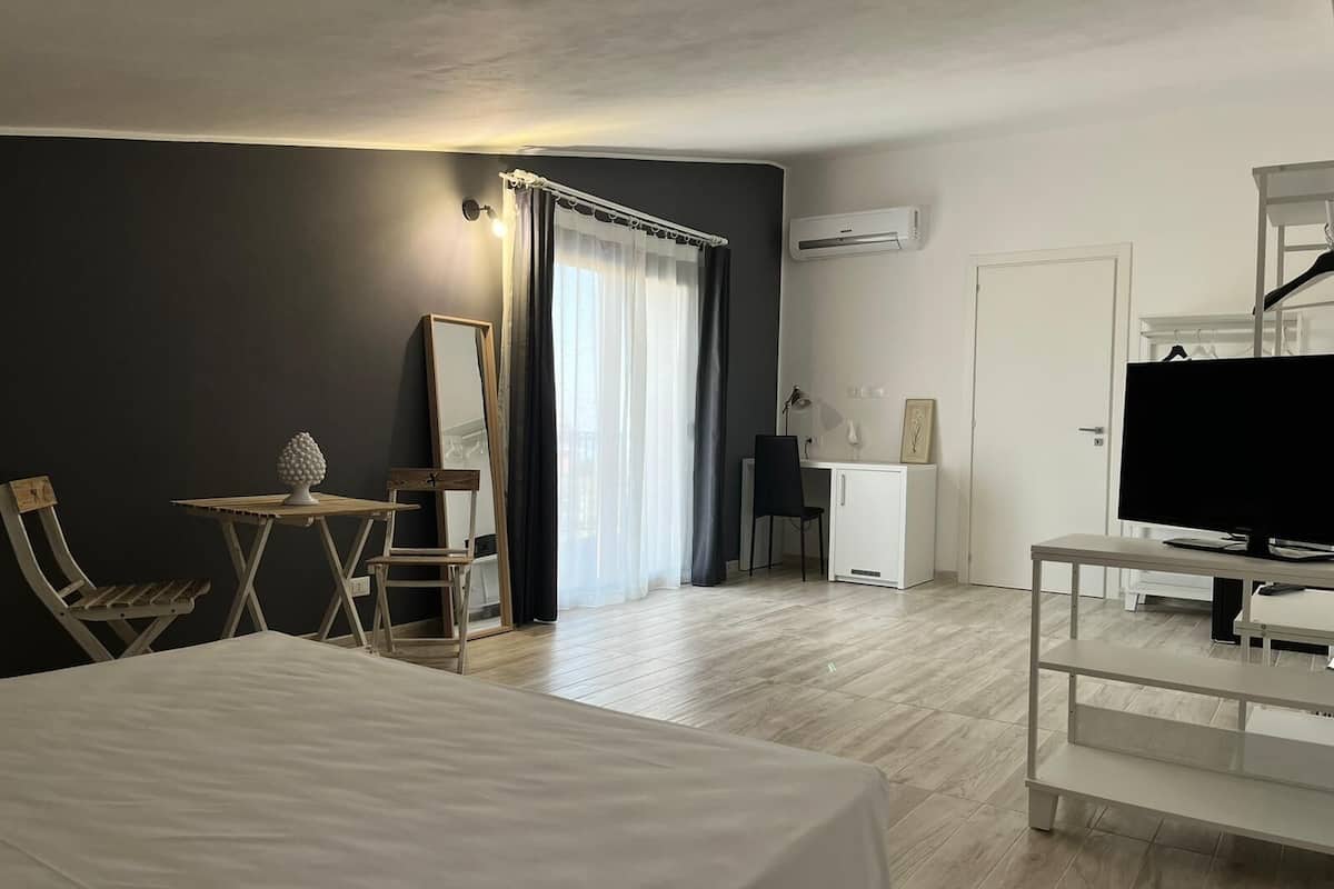 A hotel room with a bed, a desk, a chair, a TV, and an air conditioning unit.