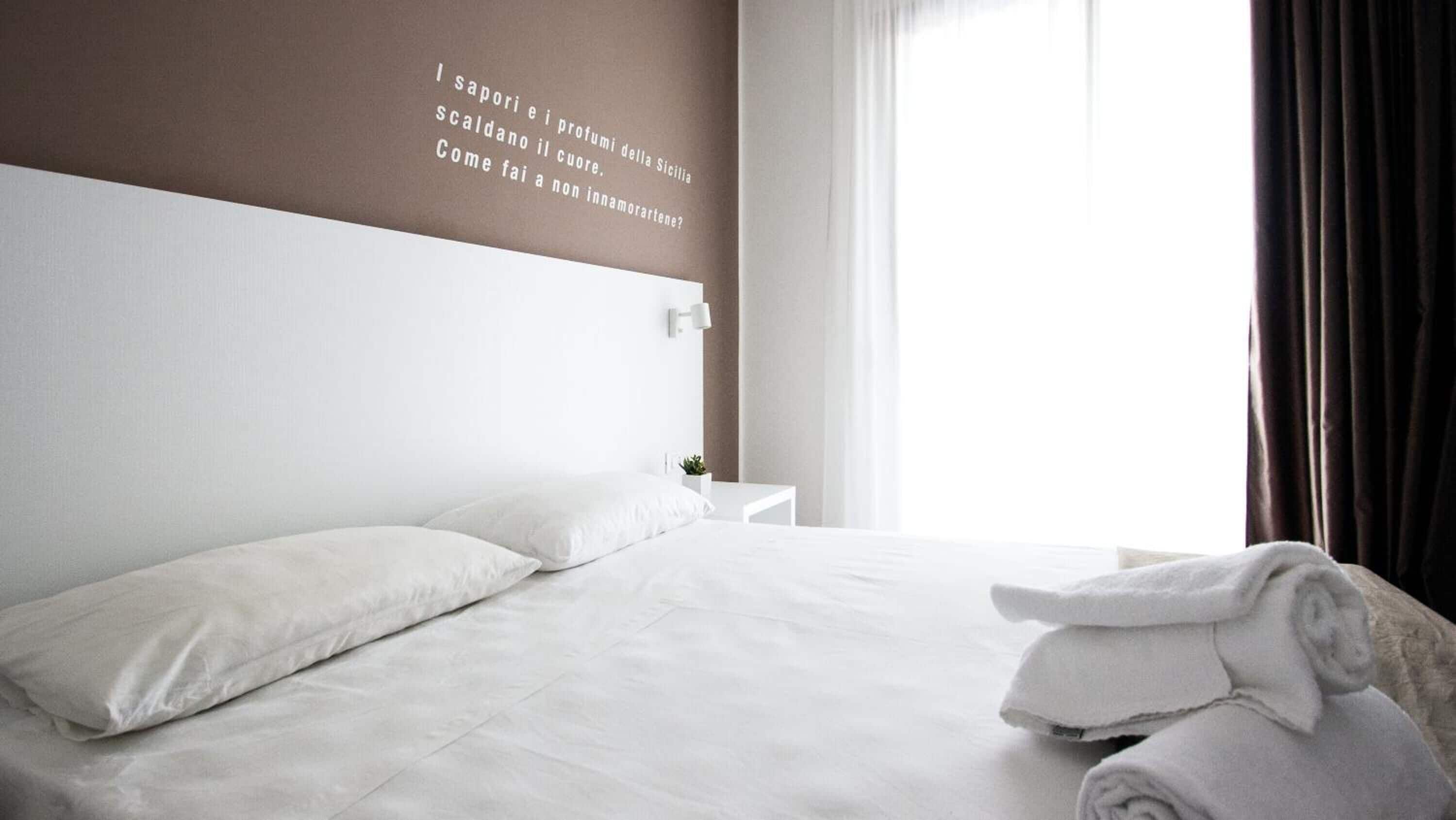 A hotel room with a neatly made bed, a bedside table with a lamp, and a view of the outdoors.