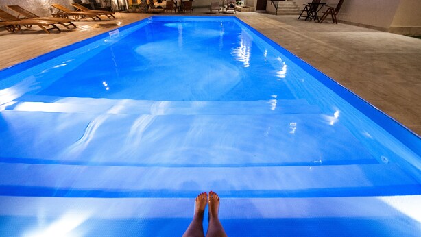 Una piscina con superficie de agua azul cristalina, sillas de descanso y suelo de baldosas.