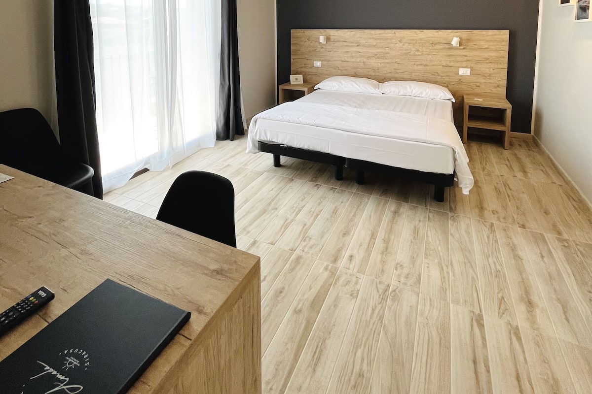 A hotel room with a bed, a desk, a chair, and a window with curtains.