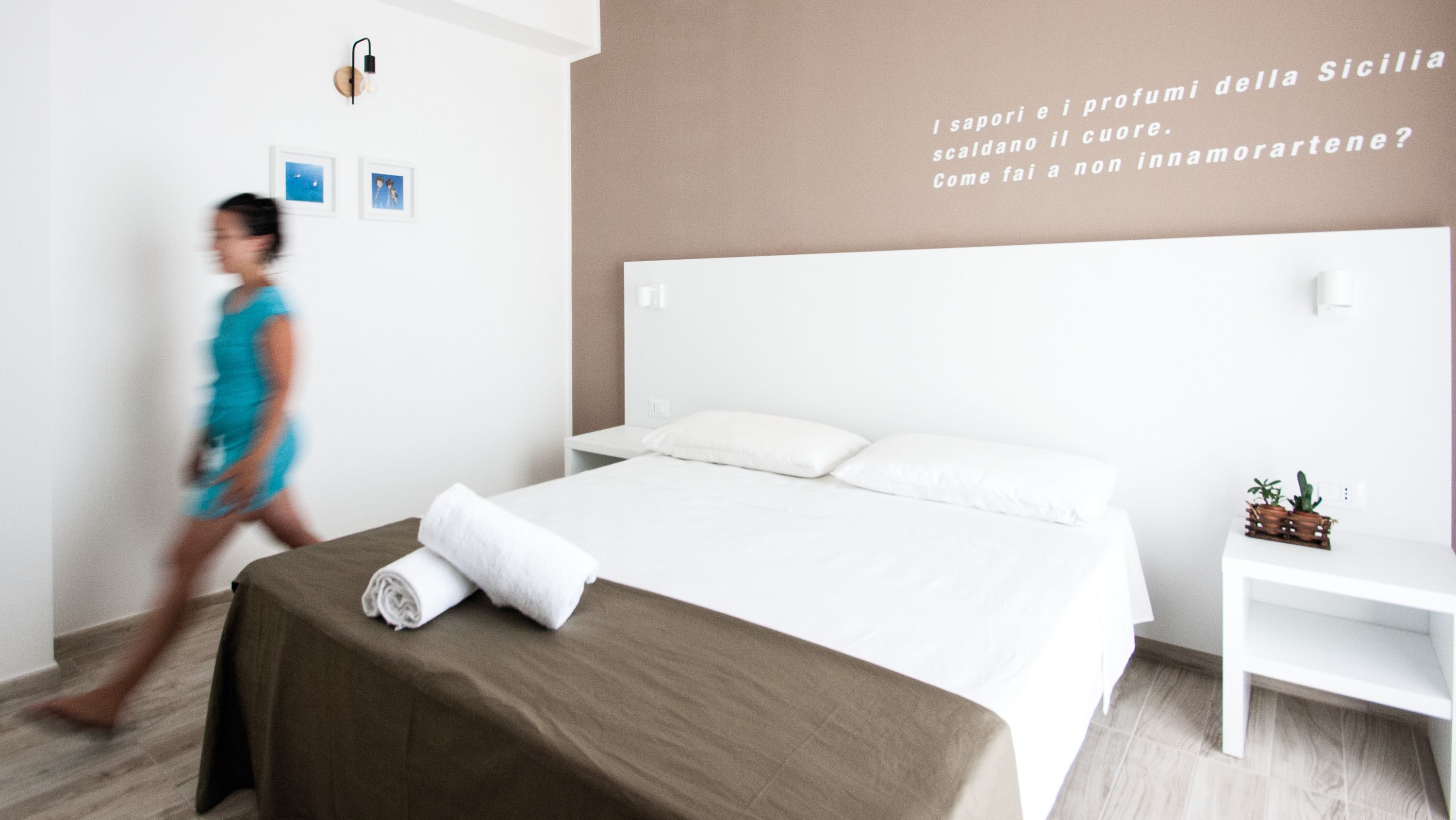 A modern hotel room with a large bed, a bedside table, and a wall with text in Italian.