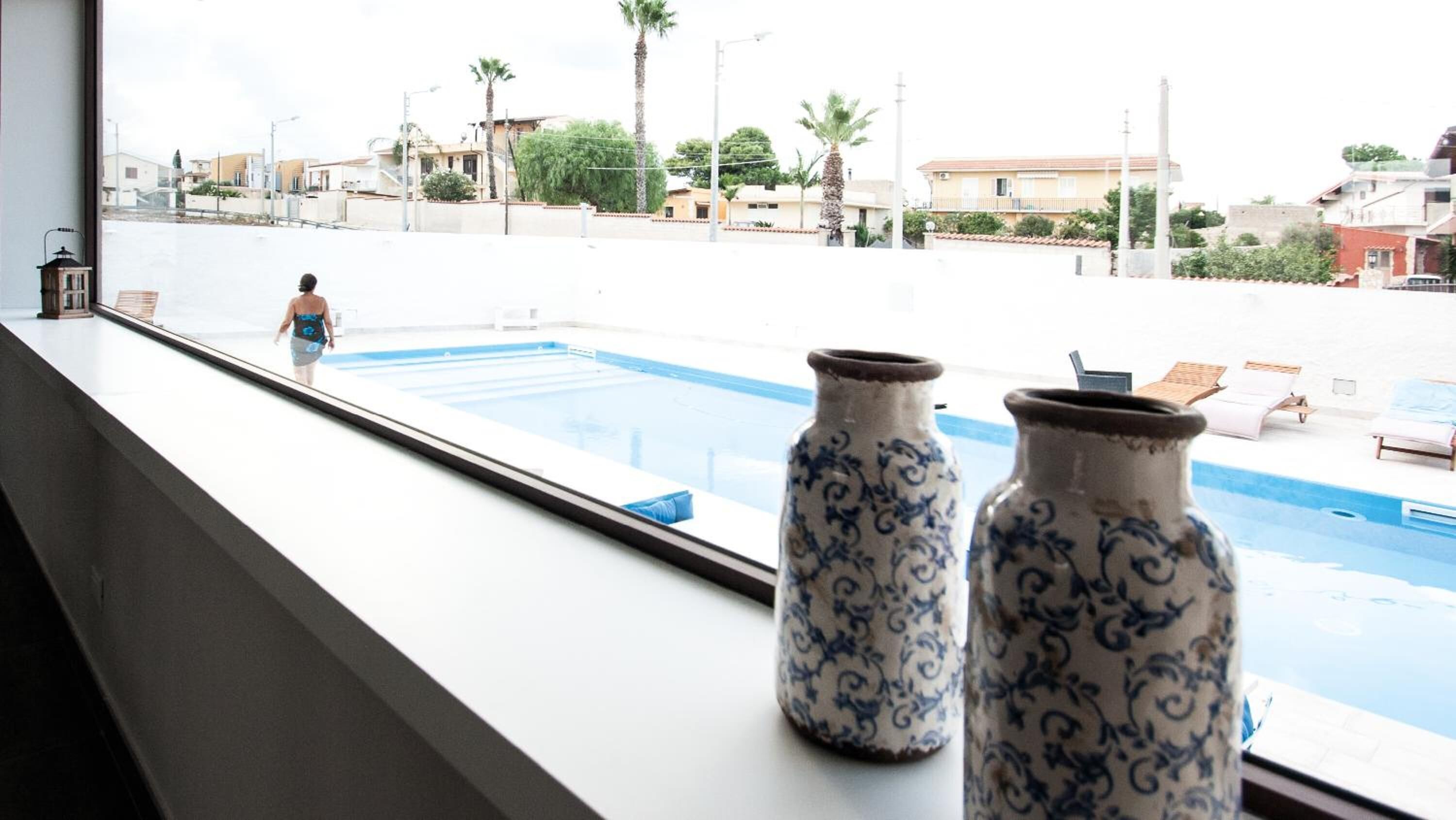 Une vue sur une piscine, prise depuis une fenêtre ornée de deux vases décoratifs posés sur le rebord.