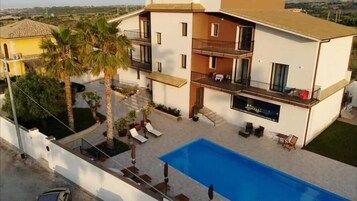 A modern two-story building with a swimming pool, balconies, and a garden area.
