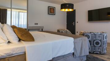 Une chambre moderne avec un grand lit, une table de chevet, une chaise, un bureau, un miroir et un téléviseur fixé au mur.