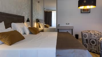 A hotel room with a large bed, a desk, a chair, and a hanging lamp.