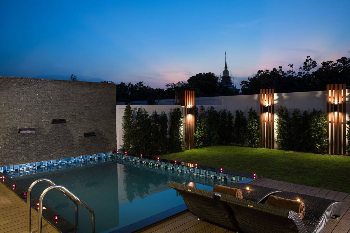 A swimming pool with a wooden deck, lounge chairs, and a brick wall.