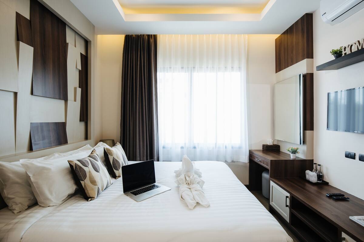 A modern hotel room with a neatly made bed, a laptop, and a desk with a mirror and a small plant.