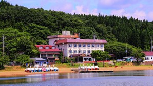 A hotel with multiple buildings, a dock with boats, and a forested hillside in the background. - Lake Side Hotel MINATOYA (Inawashiro)