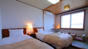 A hotel room with two beds, a nightstand, a small table, a chair, and a window with natural light. - Lake Side Hotel MINATOYA (Inawashiro)