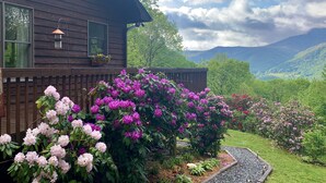 Une maison en bois ornée d’un motif solaire, avec une jardinière et un jardin où poussent des fleurs roses et violettes.