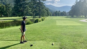 Un parcours de golf avec un étang, des arbres et des montagnes en arrière-plan.