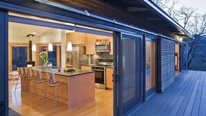 A modern kitchen with a large island, stainless steel appliances, and a sliding glass door leading to an outdoor deck.
