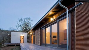 A modern house with a deck, large sliding glass doors, and a visible interior with a bed.