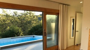 A bedroom with a large bed, a view of a swimming pool, and a sliding glass door leading to an outdoor deck.
