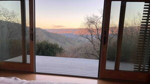 A room with a large sliding glass door leading to a deck with a view of a mountainous landscape.