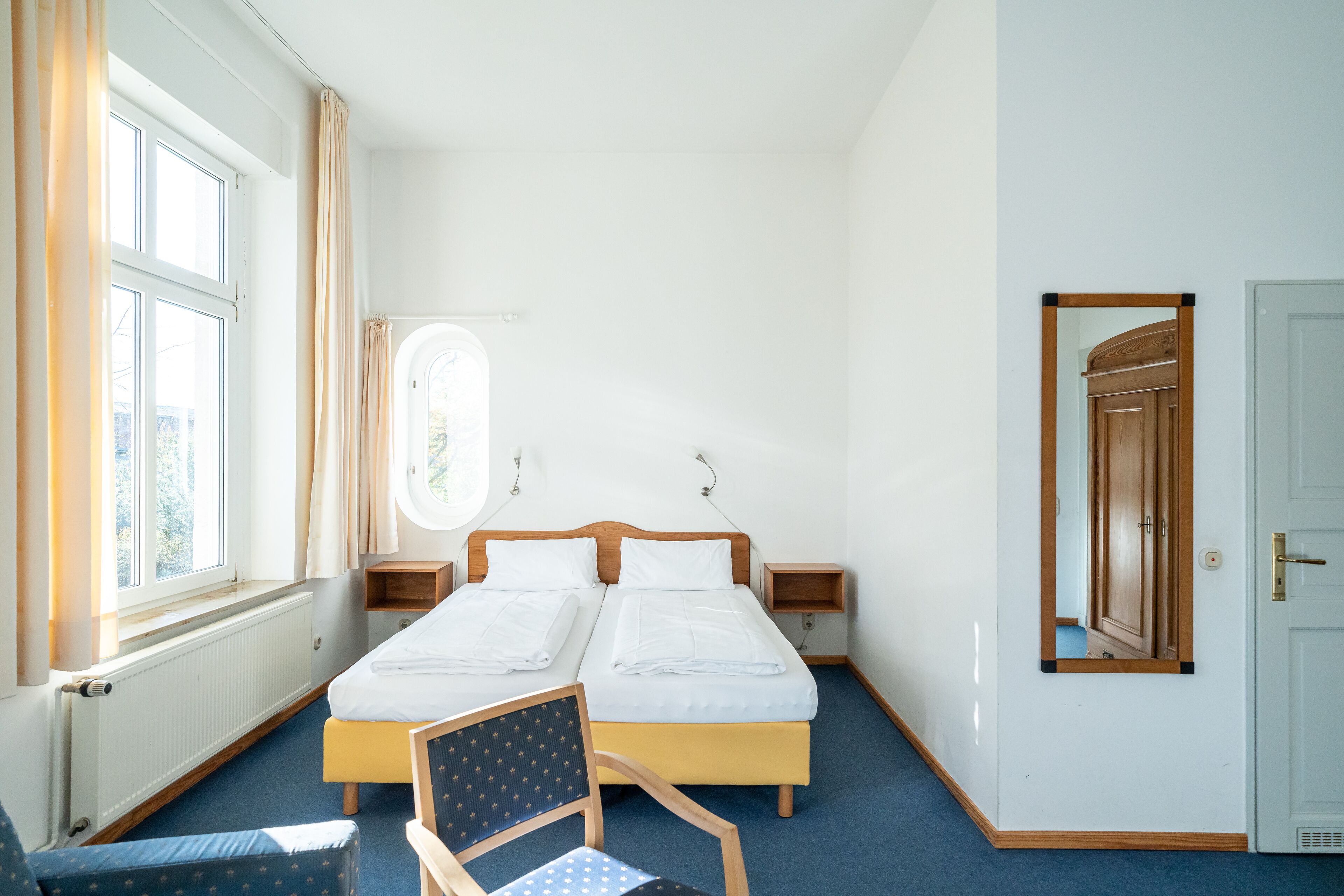 Habitación de hotel con dos camas individuales, una silla, una mesita y una ventana con cortinas.