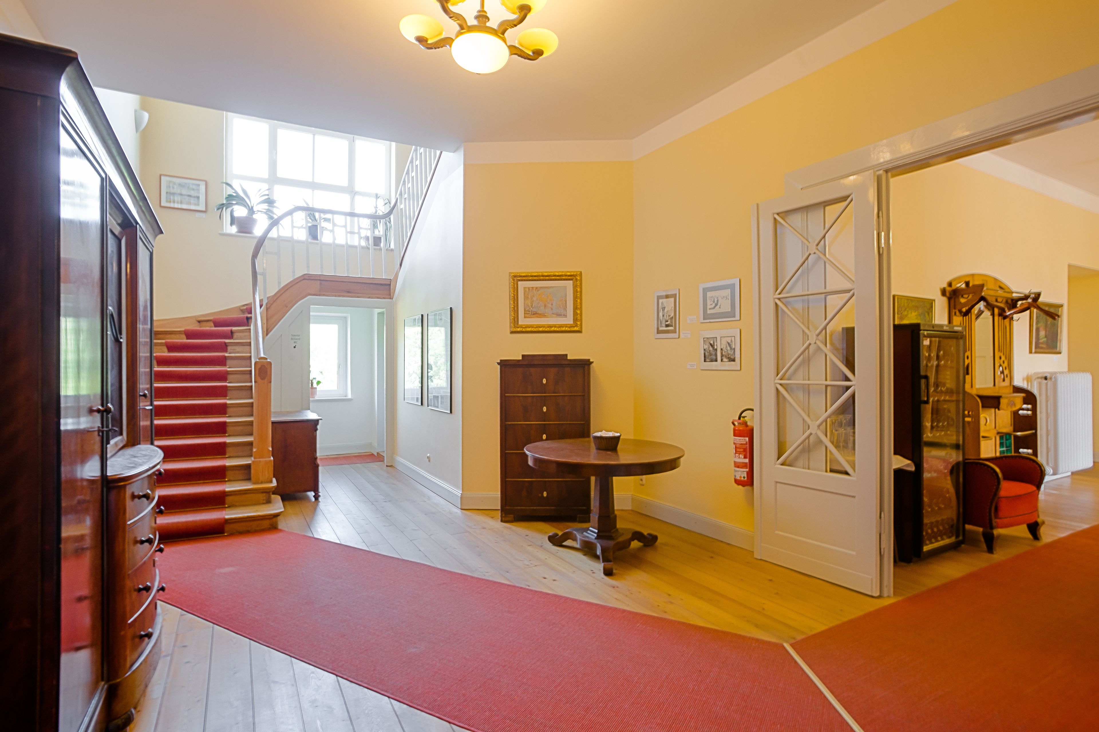 Una habitación amplia con una escalera, muebles de madera y una alfombra roja.