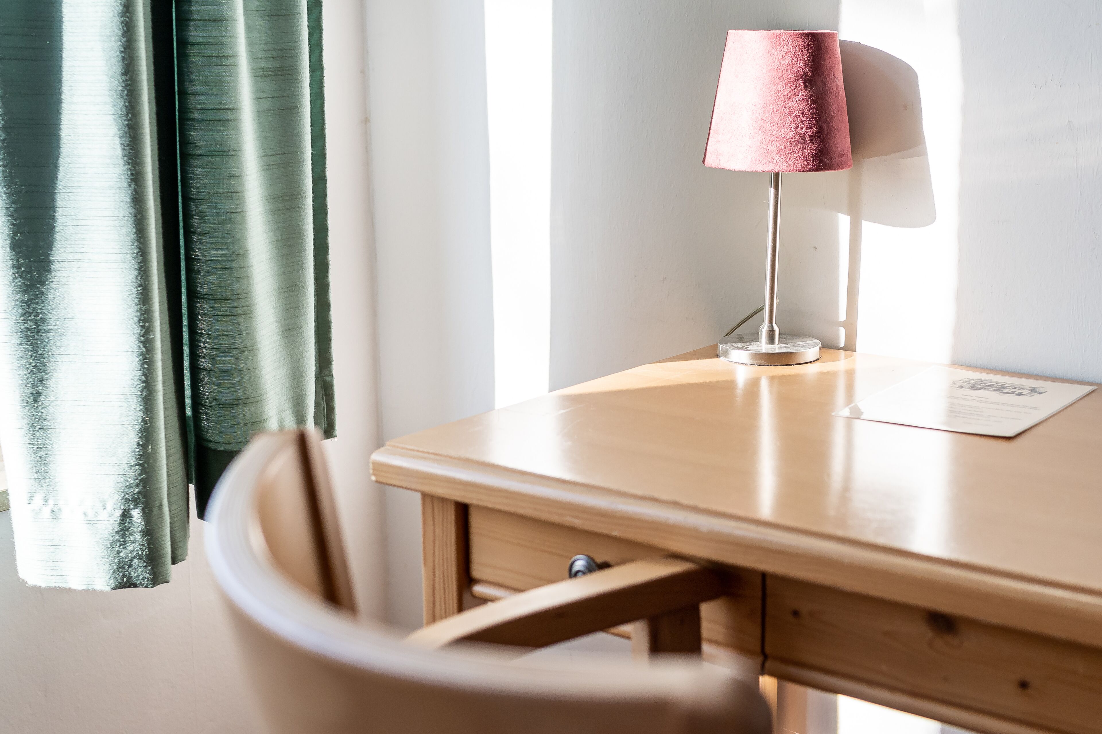 Uma escrivaninha de madeira com uma luminária, uma cadeira e uma janela com cortinas.