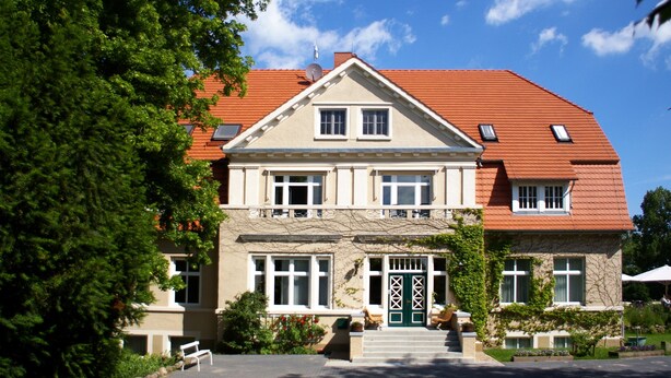 A two-story building with a red-tiled roof, multiple windows, and a green door. - Gutshaus Barkow (Barkhagen)